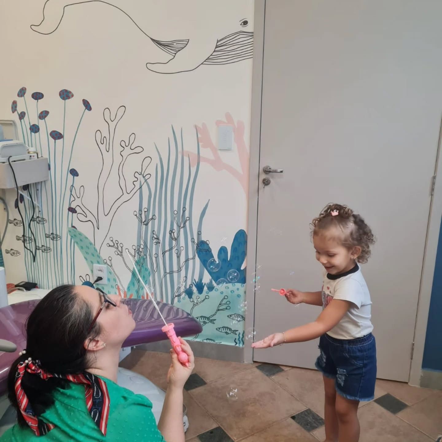 Dentista fazendo bolhas de sabão para uma menina na sala com mural do fundo do mar