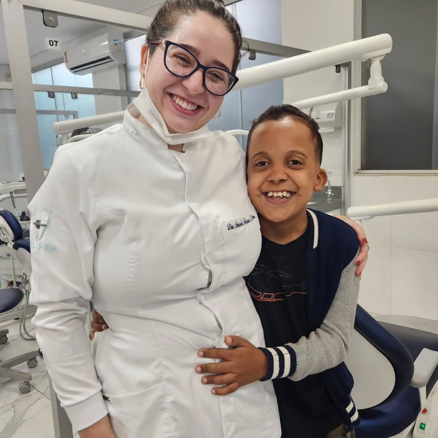 Dentista de jaleco abraçando um menino sorridente no consultório