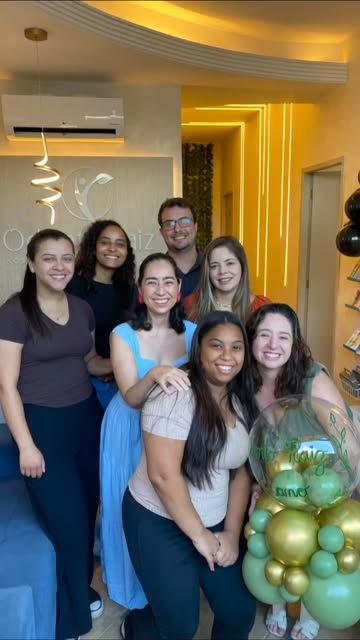 Equipe da Odonto Raiz reunida na recepção, em frente à parede com a logo, no aniversário de um ano