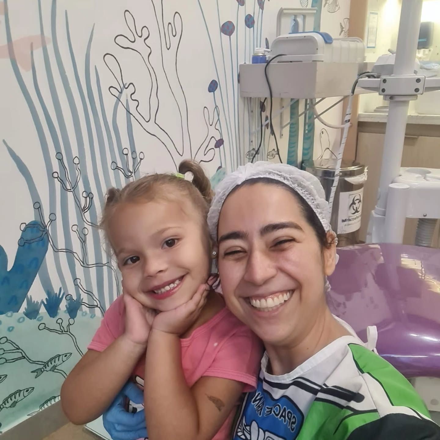 Menina sorrindo ao lado da dentista na sala infantil, com mural do fundo do mar